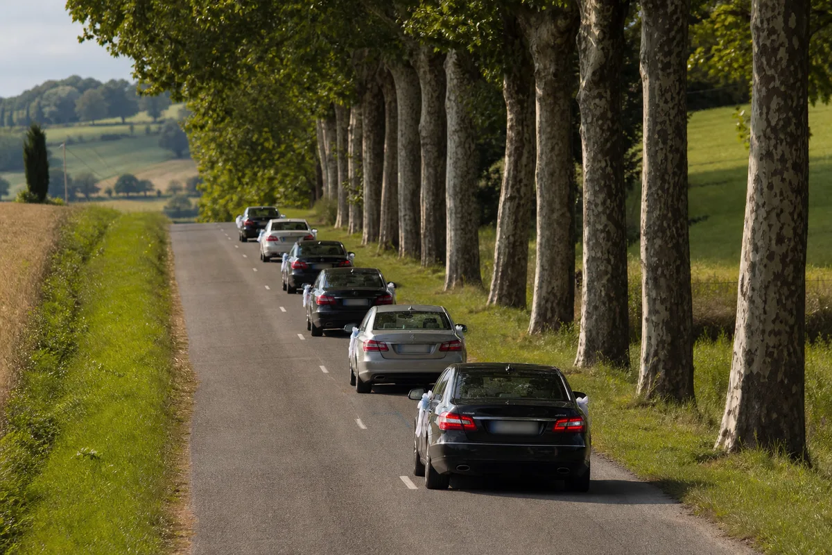 Convoi de voitures de mariage roulant en file sur une route de campagne