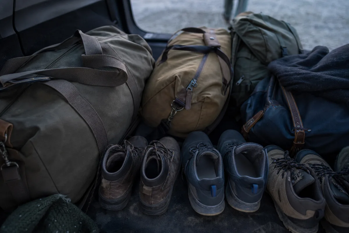 Sacs de voyage en toile et chaussures de marche alignés dans un coffre de véhicule ouvert au petit matin